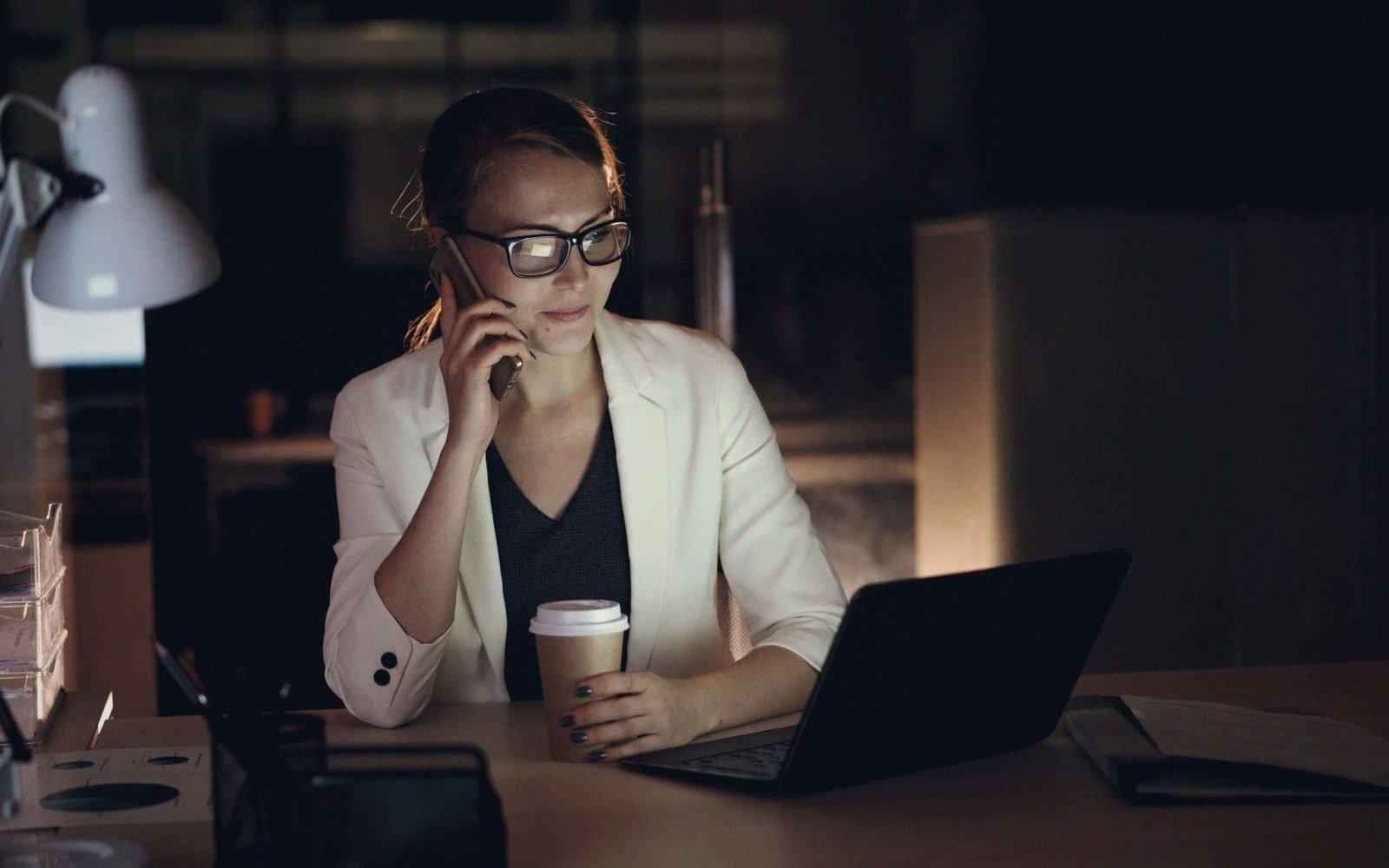 A woman alone at a desk late, the room dark behind her