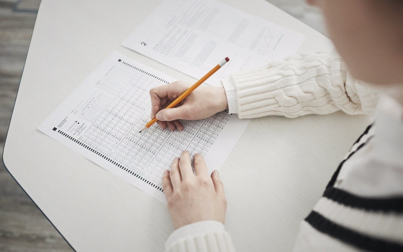 Student marks answers with a pencil on a bubble-sheet answer form at a desk