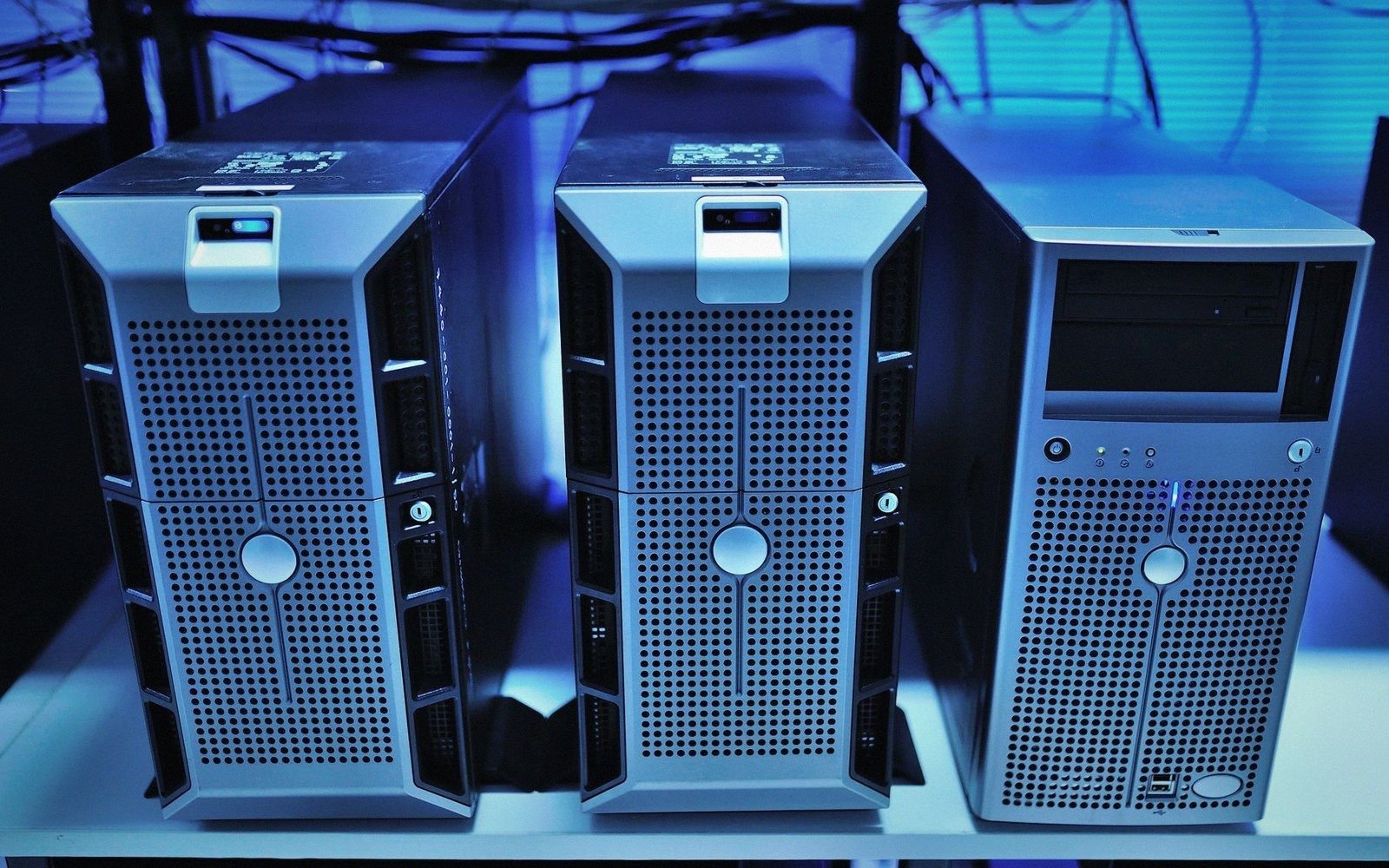 Three tower server computers with perforated front panels stand side by side in a data center