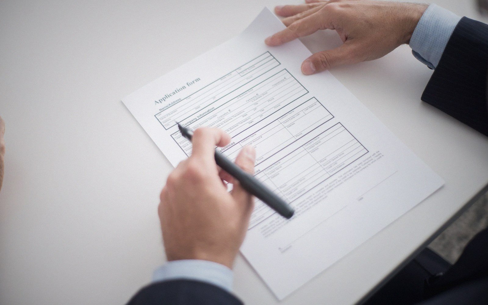 A hand holding a pen over a printed application form on a desk
