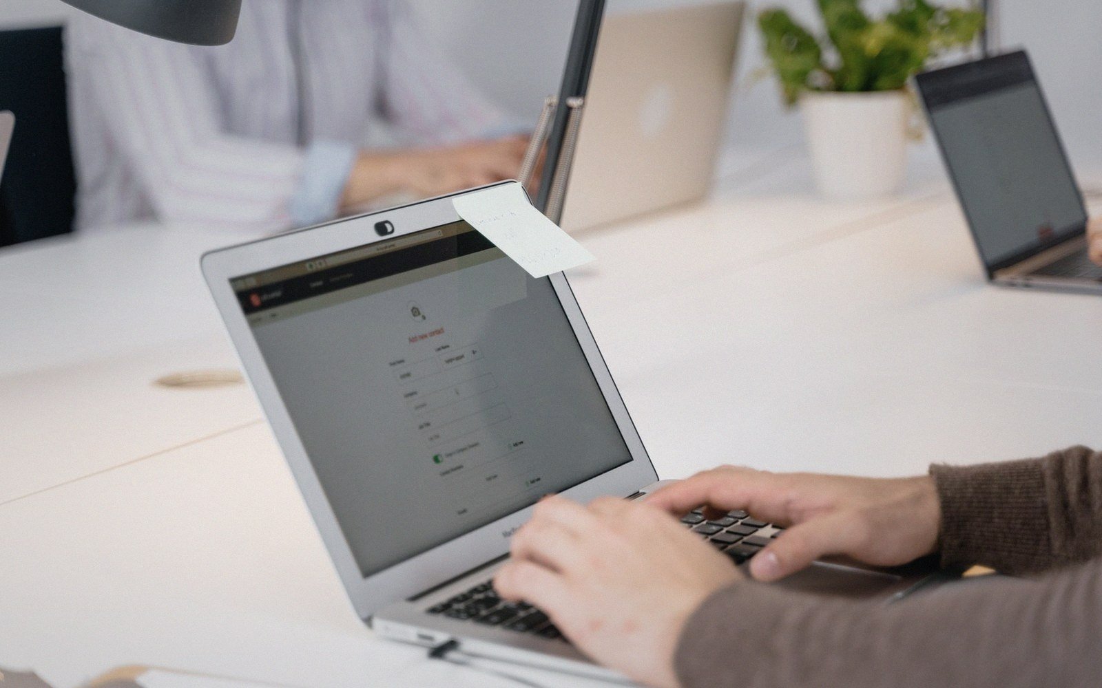 Hands typing on a laptop keyboard displaying a form on a shared office desk