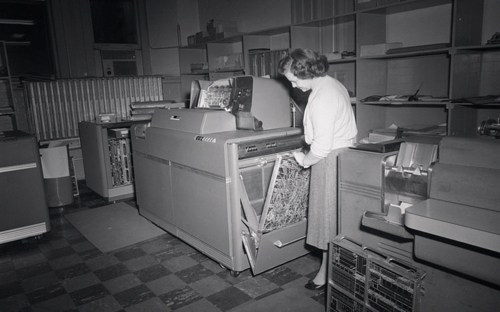A woman operates a punched-card tabulating machine in a vintage computer room